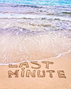 Last Minute written on sand, with waves in background, vacation concept