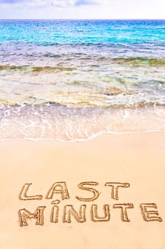 Last Minute written on sand, with waves in background, vacation concept