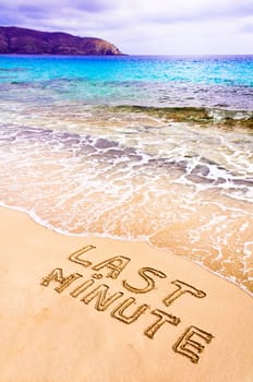 Last Minute written on sand, with waves in background, vacation concept