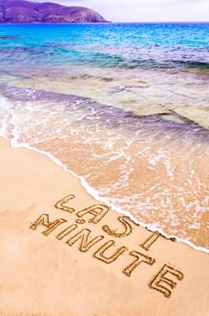 Last Minute written on sand, with waves in background, vacation concept