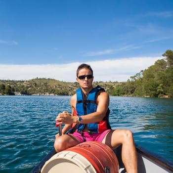 Handsome young man on a canoe on a lake, paddling, enjoying a lovely summer day