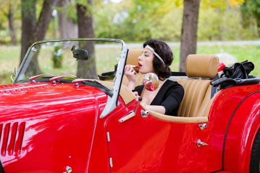 Woman stains the lips before mirror in car
