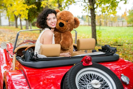 Smiling woman with bear toy in retro car