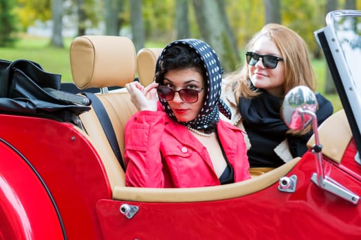 Fashionable women at retro red car look satisfied
