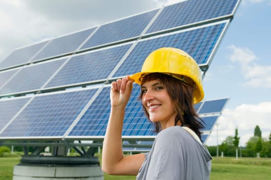 lateral head-and-shoulder portrait of a young,brunette woman with a yellow construction helmet as headgear and an optimistic look into the camera  right hand on helmet