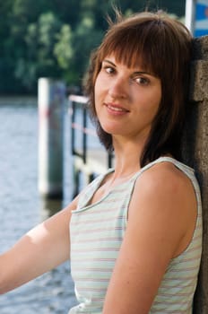 Side view Head-and-shoulder portrait of a young,brunette woman in a sleeveless top at the lake with a view into the camera