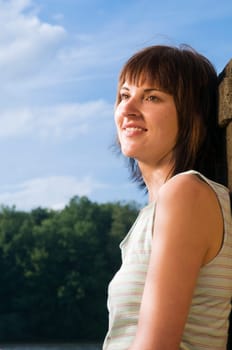 Side view Head-and-shoulder portrait of a young,brunette woman in a sleeveless top by the lake with a smiling look to the side