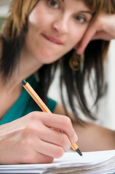 Head-and-shoulder view of a young,brunette woman sitting at the table with pen in hand and binder in front of her