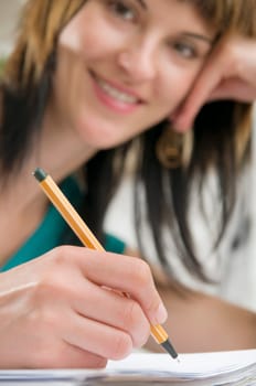 Head-and-shoulder view of a young,brunette woman sitting at the table with pen in hand and binder in front of her