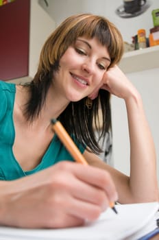 Head-and-shoulder view of a young,brunette woman sitting at the table with pen in hand and binder in front of her