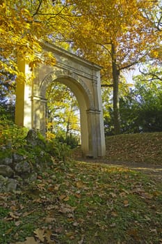 Autumn park with unknown romantic gate. Tree leaves are yellow.