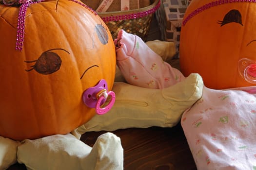 Two pumpkins dressed up as princess babies with pacifiers.
