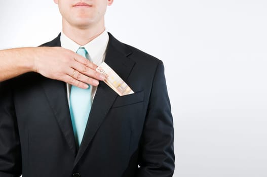 Upper body view without head of a young man in a black suit against a white background  a hand protruding into the picture from the left inserts a folded banknote into the outer breast pocket