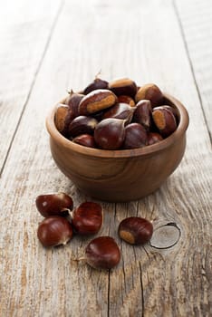 Raw chestnuts in bowl on wooden background