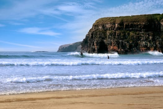 beautiful clean atlantic ocean with surfers catching the waves with cliffs in background on Irelands coast
