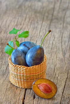 basket with plums on wooden background