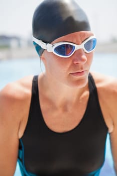 Portrait of female swimmer with goggles and black swimsuit and cap at outdoor swimming pool