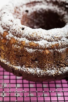 Closeup of chocolate cake sprinkled with icing sugar resting on metal grill over pink serviette with white spots