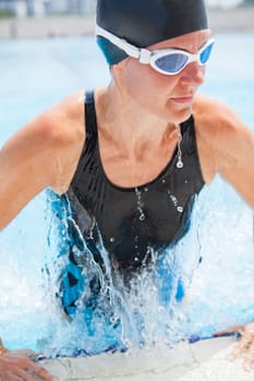 Female swimmer with black swimsuit and cap lifting herself out of swimming pool