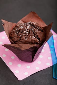 Closeup of chocolate muffin sprinkled with icing sugar resting on pink serviette with white spots