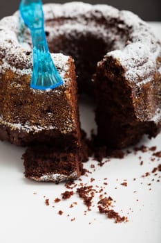 Closeup of dry chocolate cake with piece cut out sprinkled with icing sugar and blue plastic fork