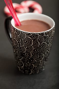 Closeup of mug of hot chocolate with red plastic spoon and hard candy heart with red swirls in background