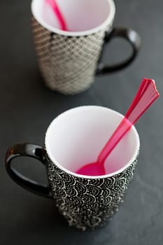 Closeup of two empty mugs with red plastic spoons on dark surface