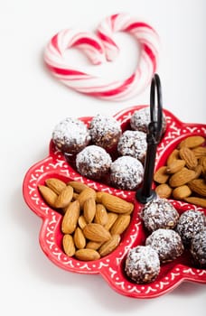 Closeup of tray of almonds and chocolate balls and hard handy heart with red swirls on light background