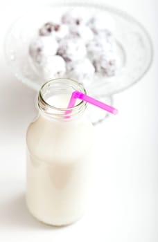 Closeup of milk in glass jar with pink straw with glass serving tray of chocolate balls sprinkled with icing sugar in background