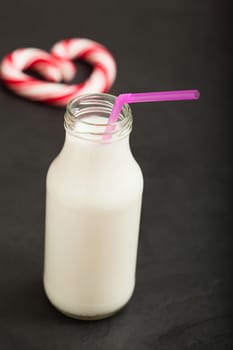 Closeup of milk in glass jar with pink straw and red candy heart in background on dark surface
