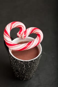 Closeup of mug of hot chocolate with hard candy heart with red swirls resting on top