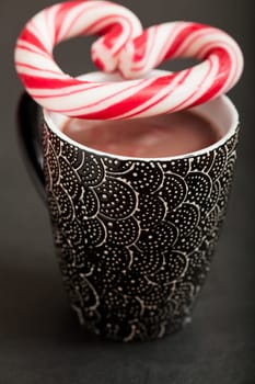 Closeup of mug of hot chocolate with hard candy heart with red swirls resting on top