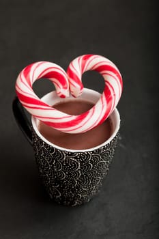Closeup of mug of hot chocolate with hard candy heart with red swirls resting on top