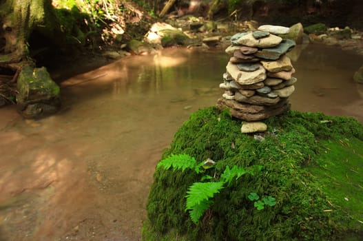 Cairn on a stone with moss and fern by a river