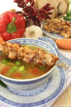 a bowl with poultry consommé and a chicken skewer
