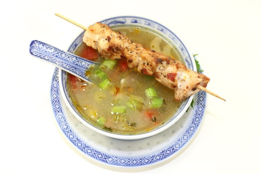 a bowl with poultry consommé and a chicken skewer
