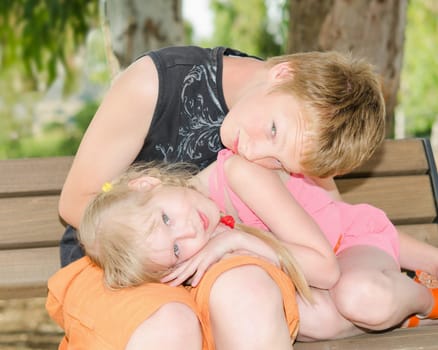 Two kids brother and sister curled up together on the bench in park