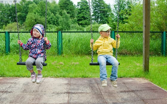 Young children, a boy with a girl swinging on a swing