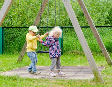 Young children, a boy with a girl swinging on a swing