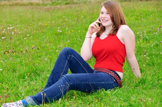 Young girl teenager with phone sits on the lawn
