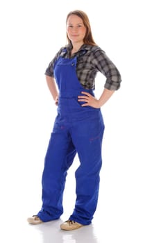 Young woman (craftswoman,do-it-yourselfer,trainee) with long hair wears a checkered blouse and blue work dungarees against a white background. She poses proudly and contentedly in front of the camera
