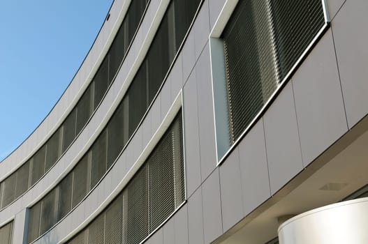 Modern façade of a commercial building with grey metal cladding and aluminium blinds against a blue sky.