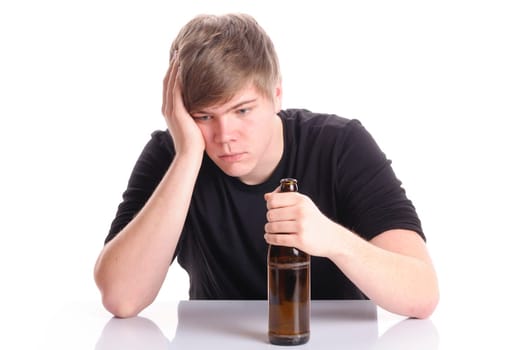 Young man with short blond hair and a black T-shirt sits at a table and holds an empty beer bottle in his hand,isolated against a white background.