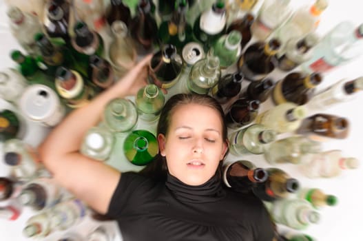 Young woman with jeans and T-shirt sits on the floor with many empty beer bottles and is drunk,photographed from above,isolated against a white background