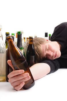 Young man with short blond hair lies on the floor and is surrounded by many empty beer and schnapps bottles,isolated against a white background.