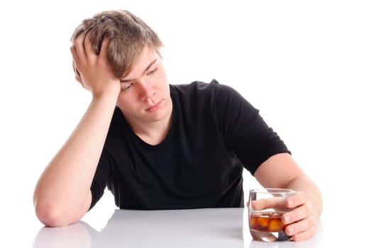 Young man with short blond hair and a black T-shirt sits at a table and holds glass of brandy in his hand,insulated against a white background.