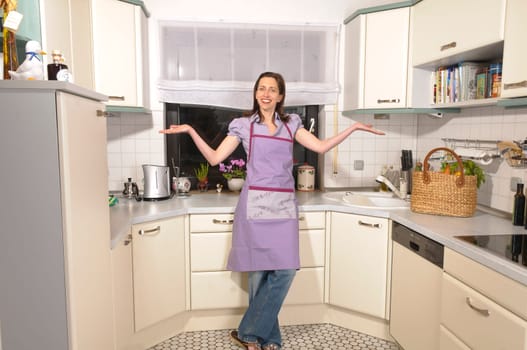 Adult housewife stands in her bright fitted kitchen and is proud and satisfied.