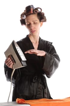 Adult housewife with curlers in her hair and a bathrobe stands behind the ironing board and irons with the iron against a white background.