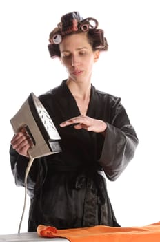 Adult housewife with curlers in her hair and a bathrobe stands behind the ironing board and irons with the iron against a white background.