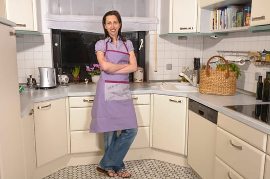 Adult housewife stands in her bright fitted kitchen and is proud and satisfied.